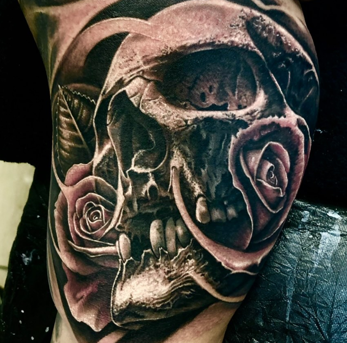 Plastisches Black-and-Grey Tattoo eines menschlichen Totenkopfs mit detaillierter Knochenstruktur, verwoben mit blühenden Rosen, feinen Blättern und geschwungenen, organischen Elementen mit hohen Kontrasten.